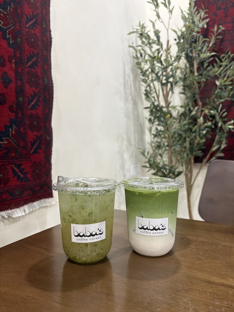 A Lemon Mint Refresher and an iced matcha on a wood table, the deep-red Afghan rug and an olive tree behind.