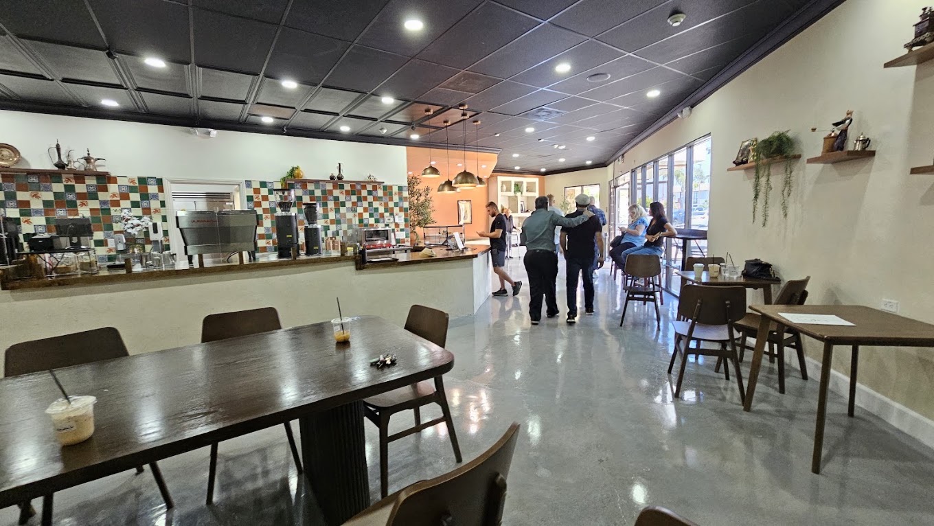 Inside Baba's — the hand-tiled espresso wall in green and terracotta, a chrome espresso machine, a long communal table and warm plaster walls.